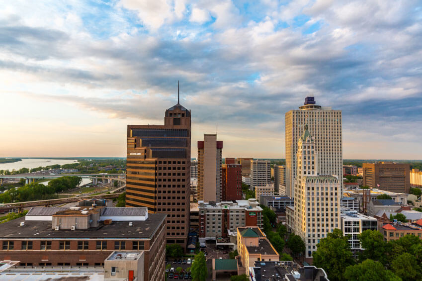 Aerial view of a cityscape featuring several tall buildings with a river and bridges visible in the background under a partly cloudy sky.
