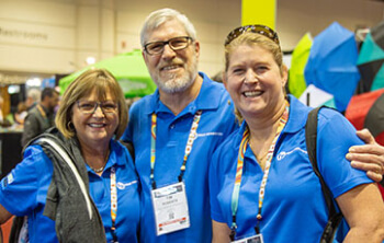 Three people in matching blue shirts at an event, smiling for the camera. Three people in matching blue shirts at an event, smiling for the camera.